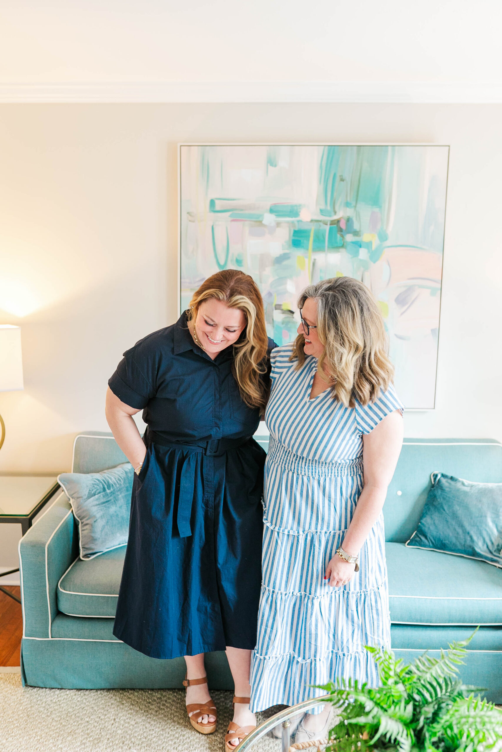 two women in a charleston home with a blue couch. both women are in blue dresses