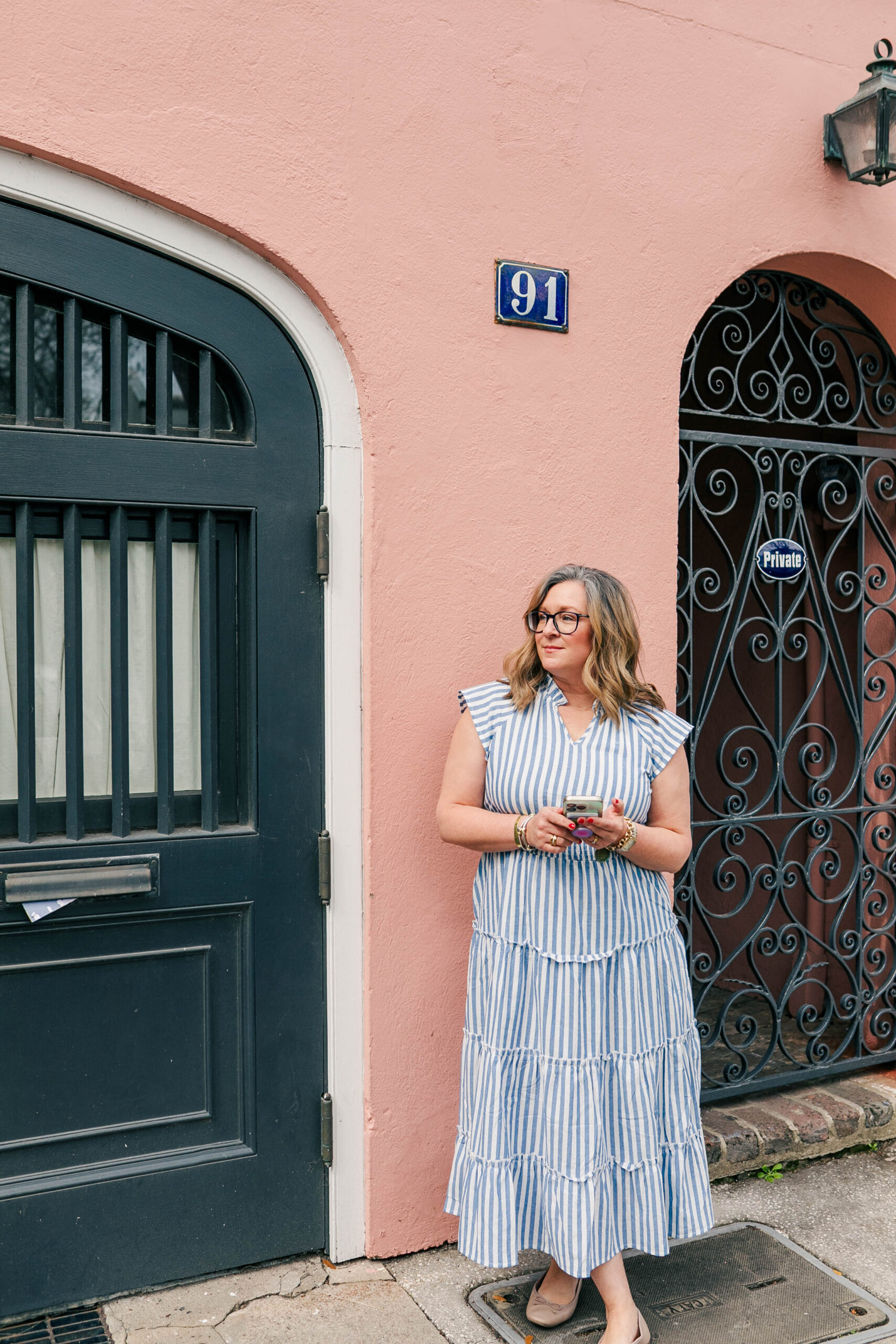 lady in blue striped dress standing front of gated door and pink building
